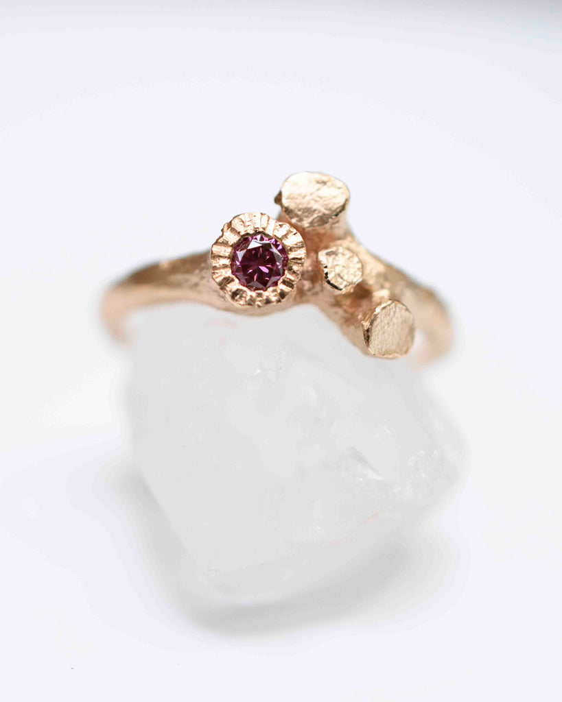 alternative rose gold ring shaped like a twig with trunks or roots, holding a pink diamond. the ring has a rough skin.